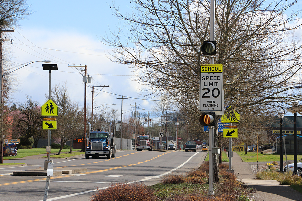A road with school zone speed limit signs and trucks driving on the road.