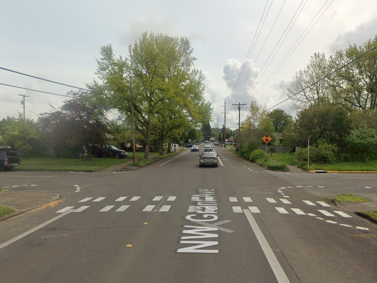 A neighborhood street intersection with a dashed, white-striped crosswalk and a caution sign on the right.  