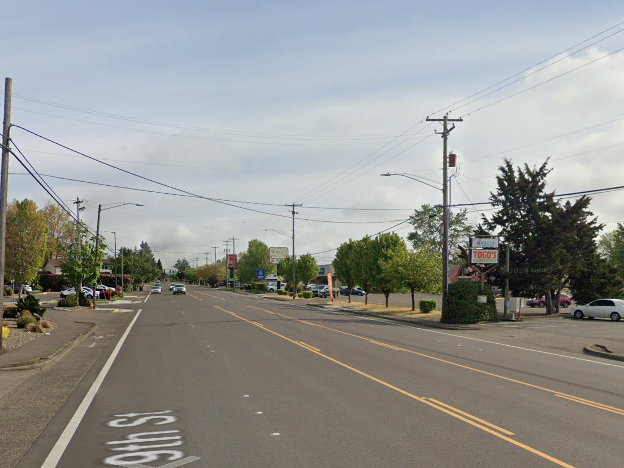 An empty five-lane road lined with utility poles, trees, business signs, and businesses driveways. 