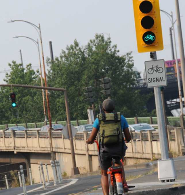 A cyclist bikes across an intersection with a traffic signal showing a green bicycle symbol.