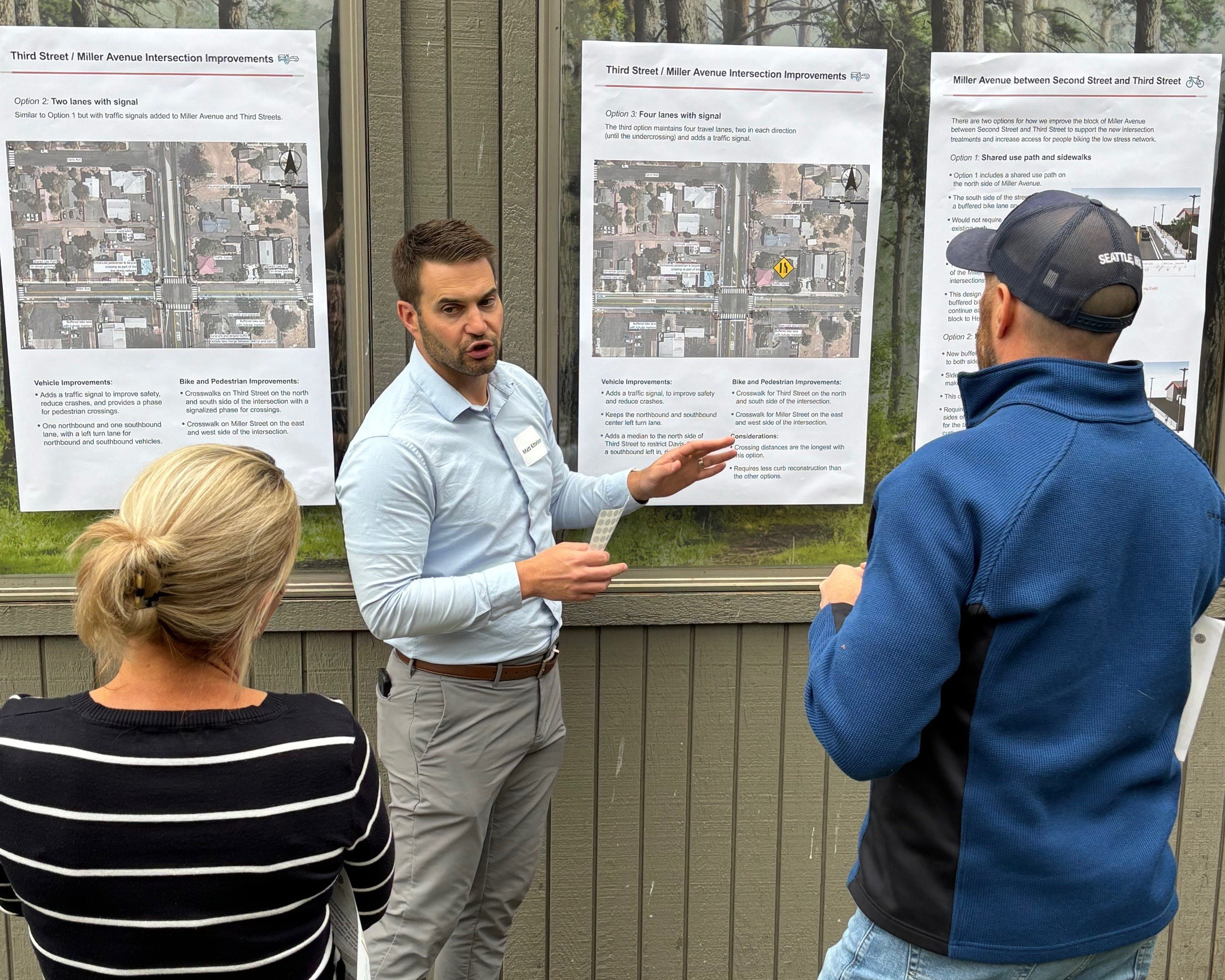 Project staff member gestures toward display boards while speaking with two community members at the first Aune Safety and Connectivity open house.