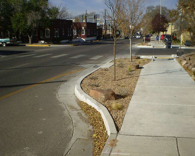 A street intersection with extended curbs that narrow the roadway at the crosswalk, reducing pedestrian crossing distance.
